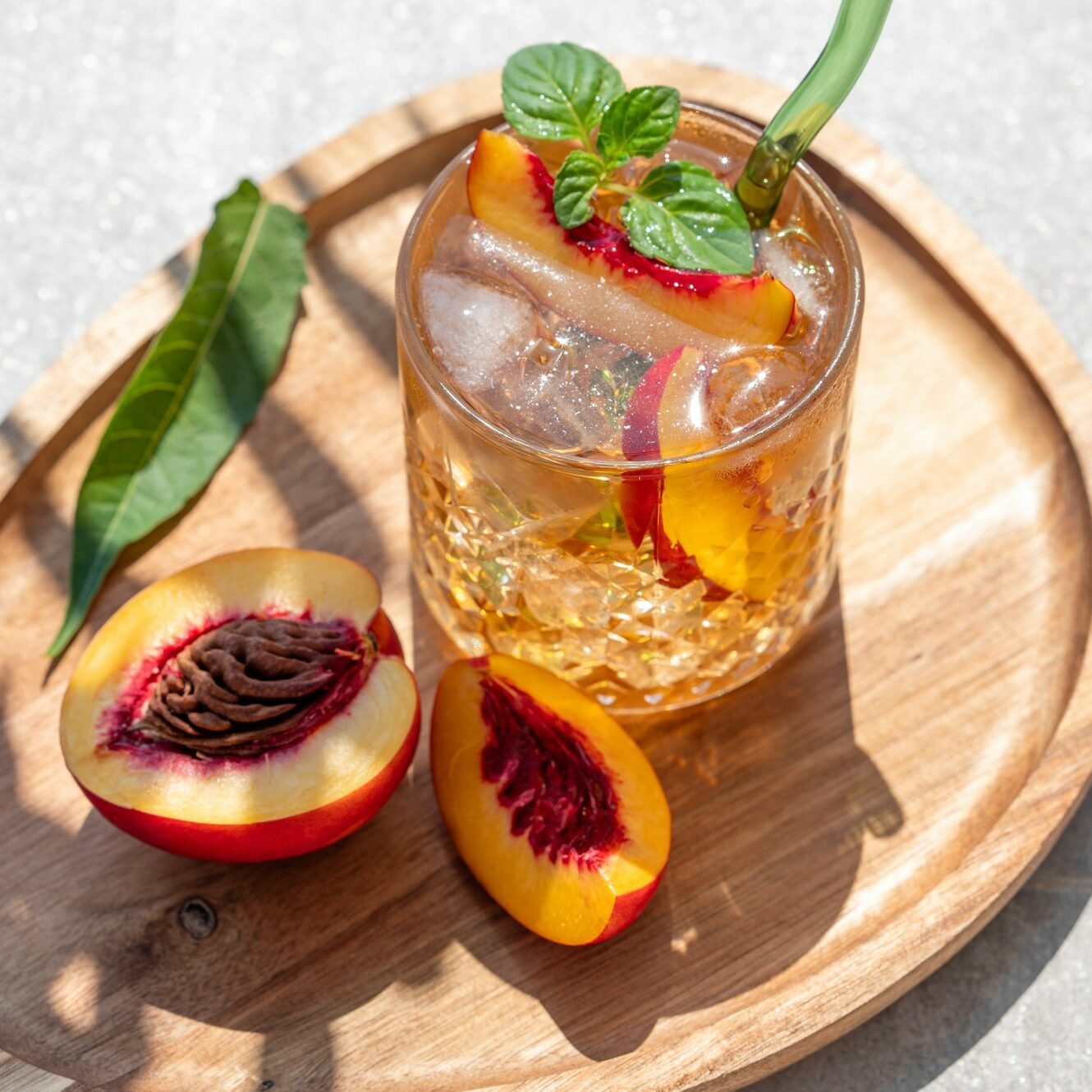 Peach lemonade with ice and mint on a wooden board on a concrete background.