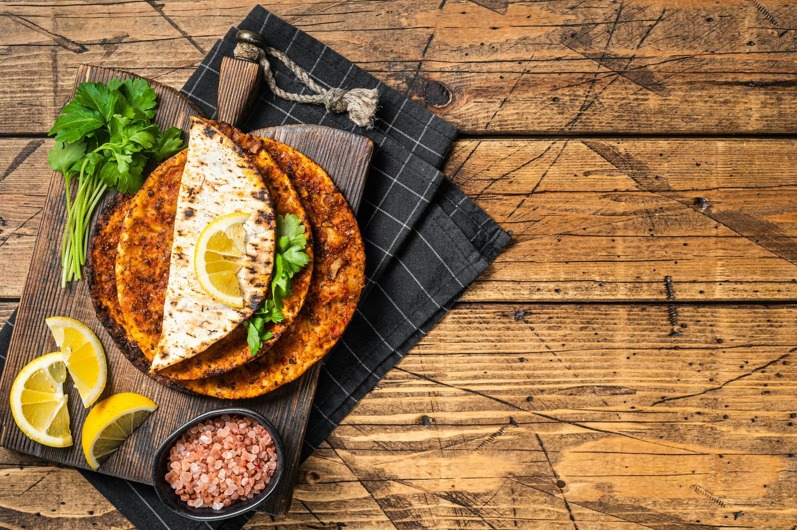 Turkish cuisine made with thin dough and minced beef meat lahmacun on wooden board with herbs.