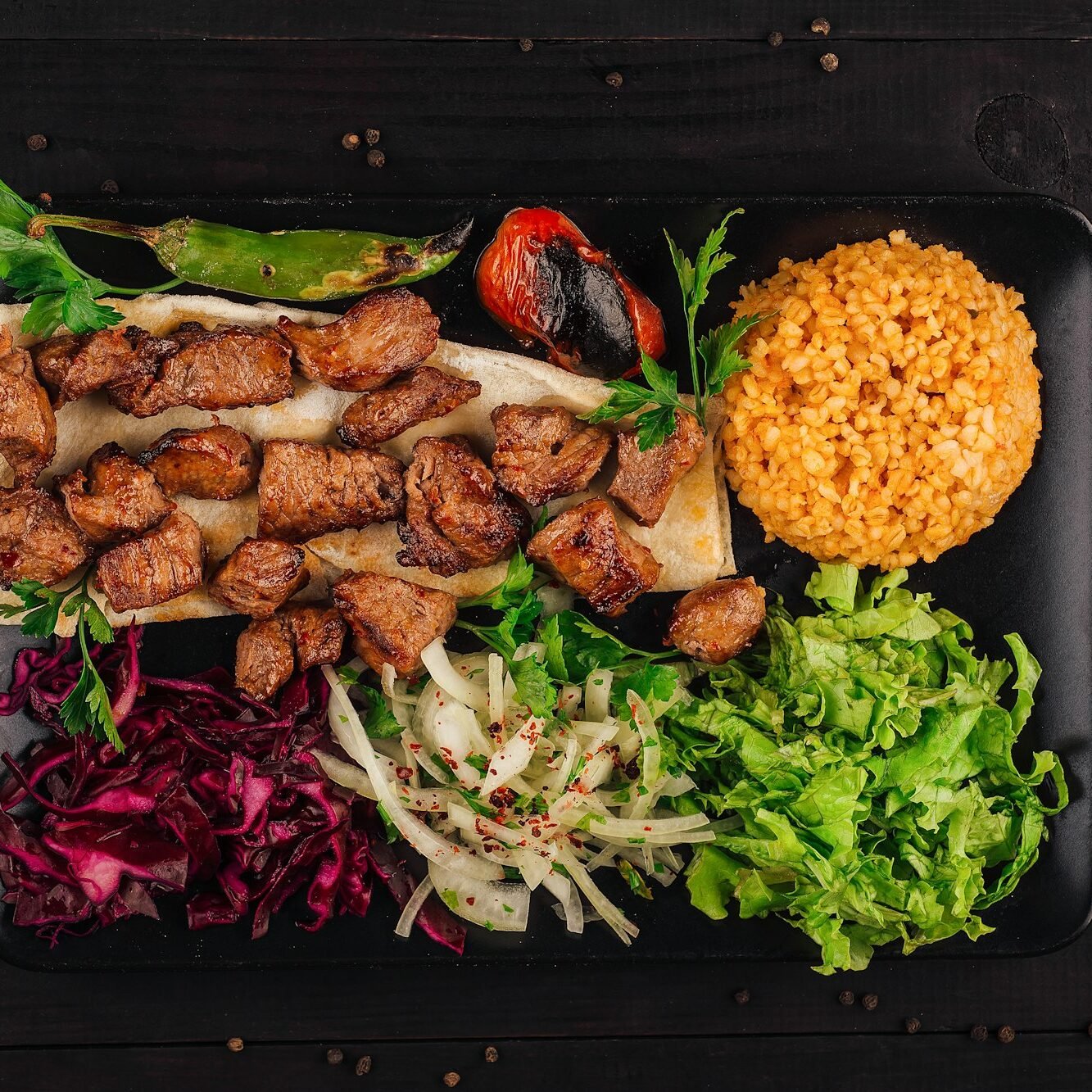 Turkish cuisine: traditional shish kebab with bulgur and vegetables on a black plate